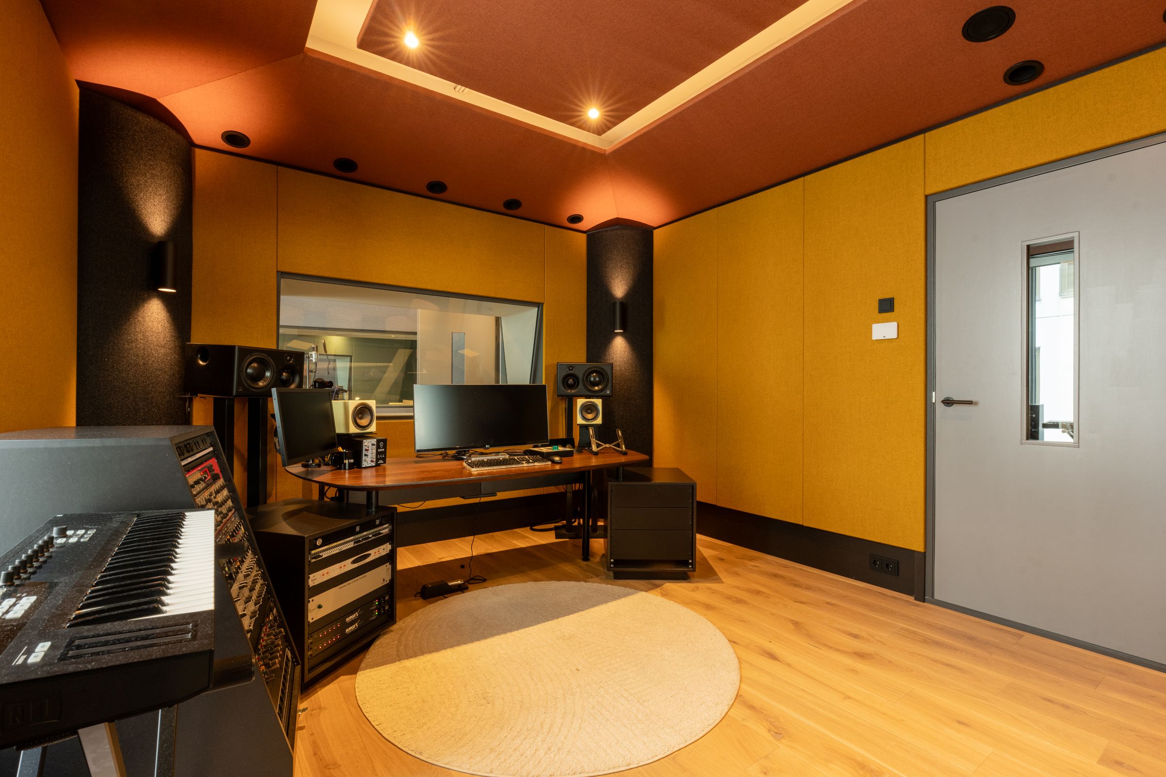 Studio van TFA met oranje en gele wanden, een regietafel, studiomonitoren en een rond tapijt
