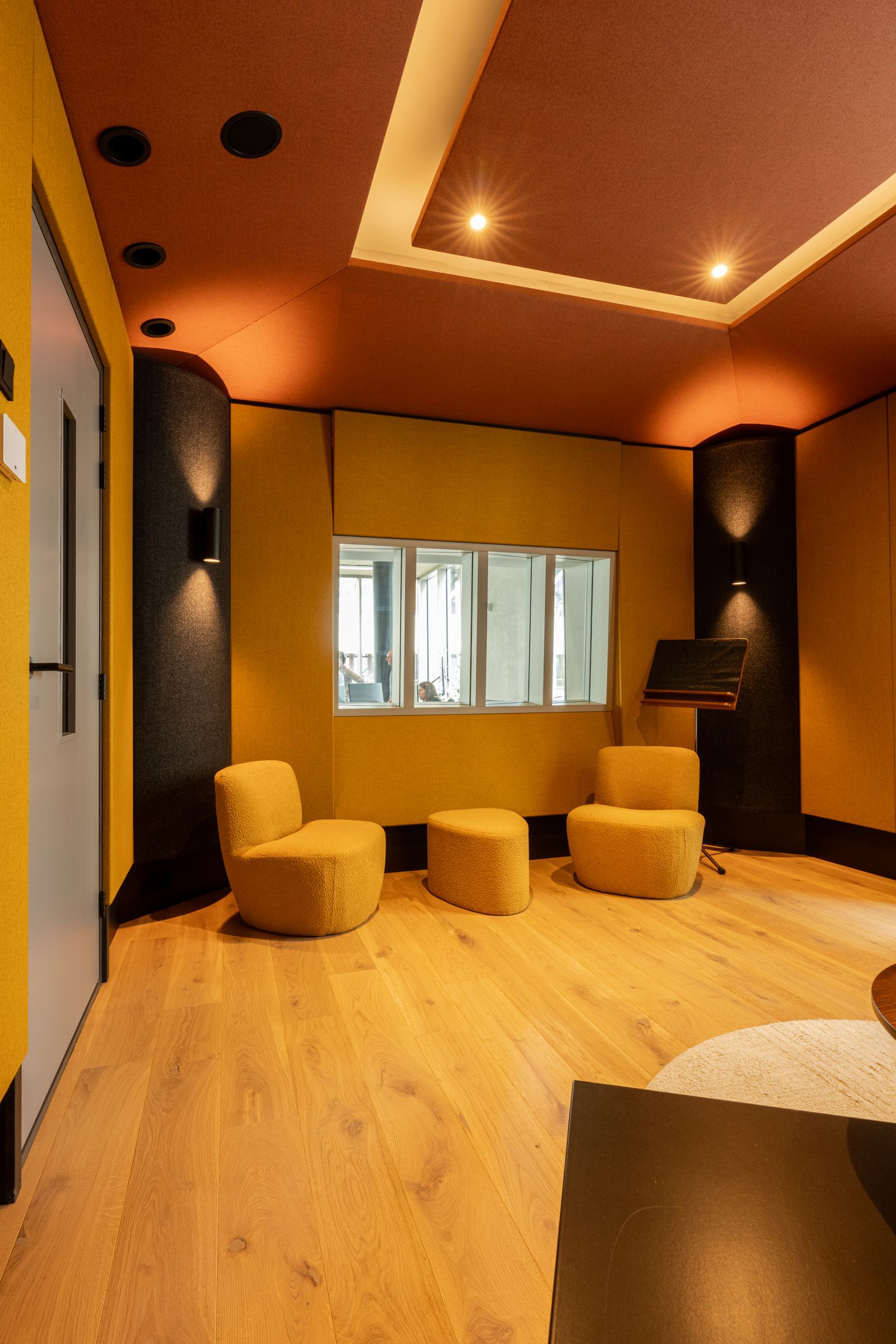Studio van TFA met oranje en gele wanden, een regietafel, studiomonitoren en een rond tapijt