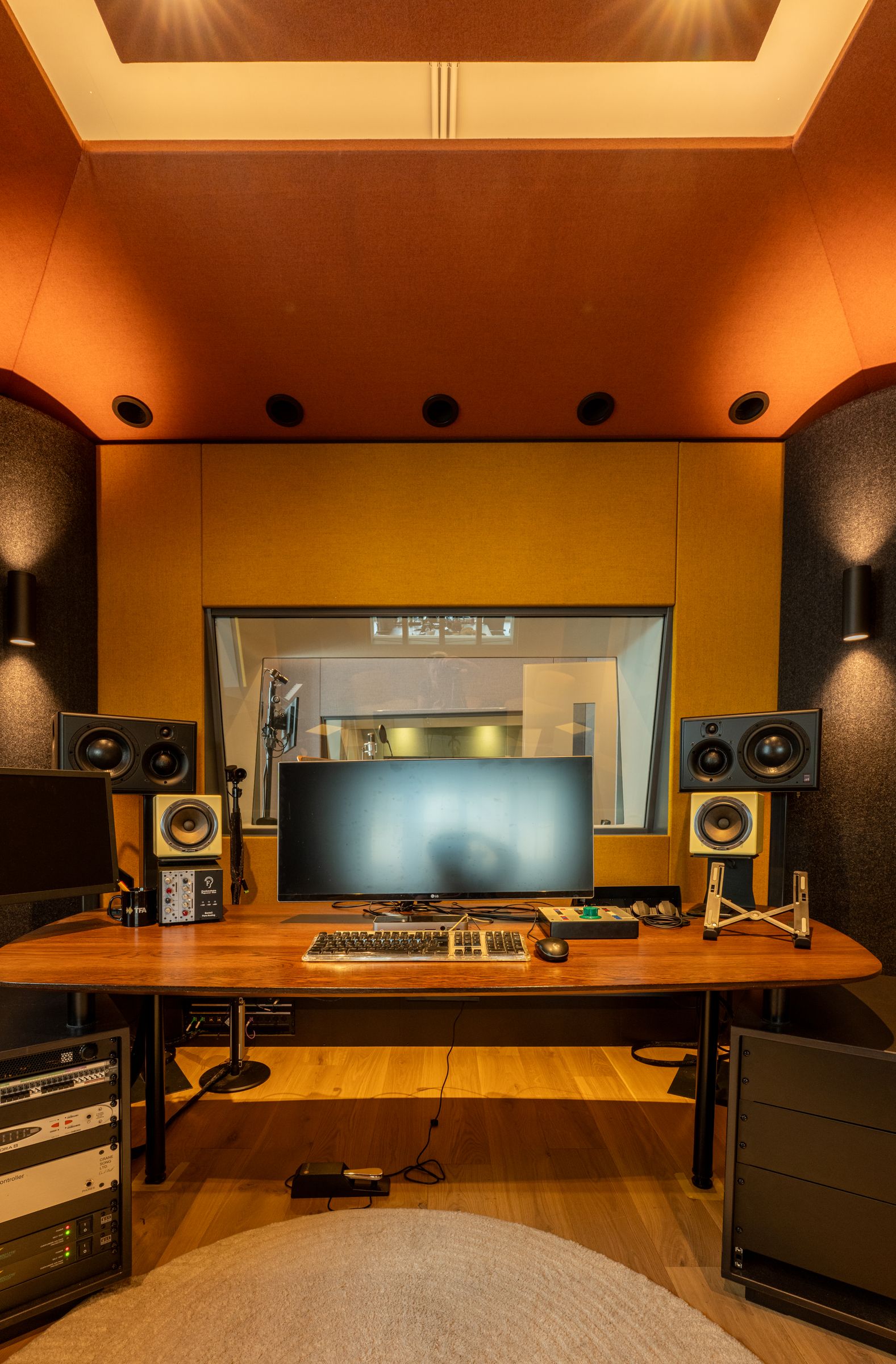 Studio van TFA met oranje en gele wanden, een regietafel, studiomonitoren en een rond tapijt