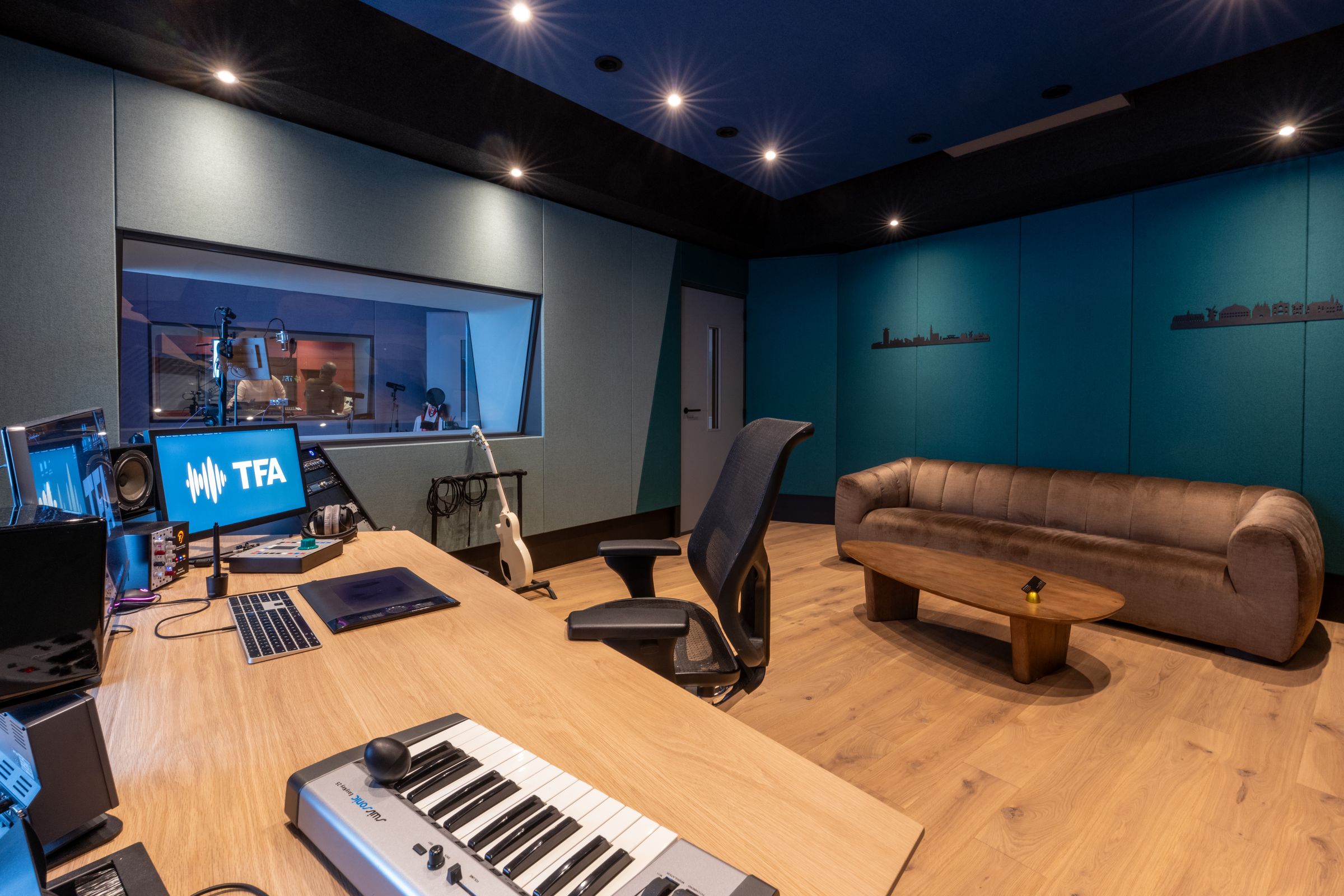Regiekamer van TFA met petrolblauwe wanden, een keyboard, studiomonitoren en een bruine bank
