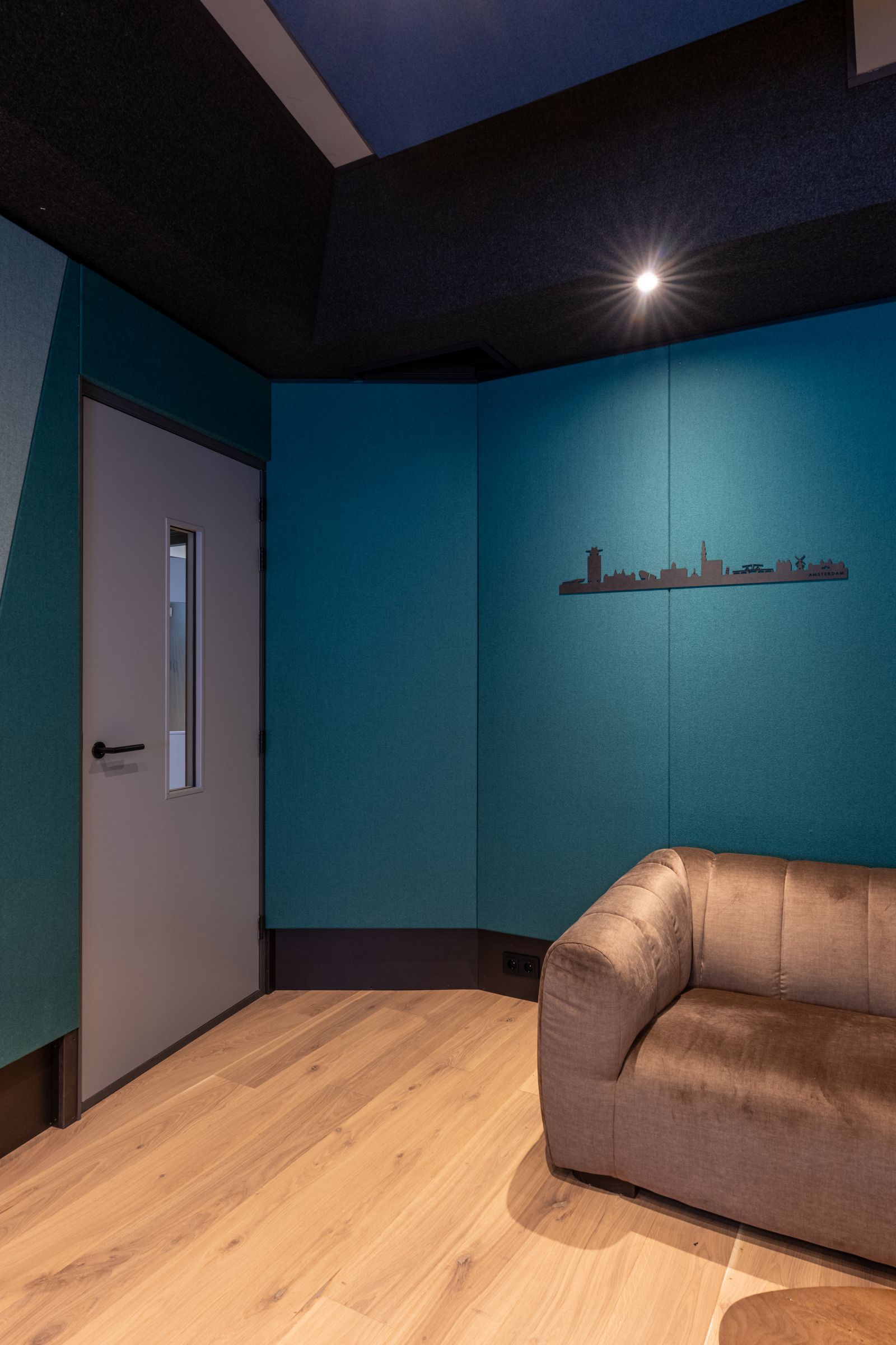 Petrolblauwe studio van TFA met een bruine leren bank en een regiestoel