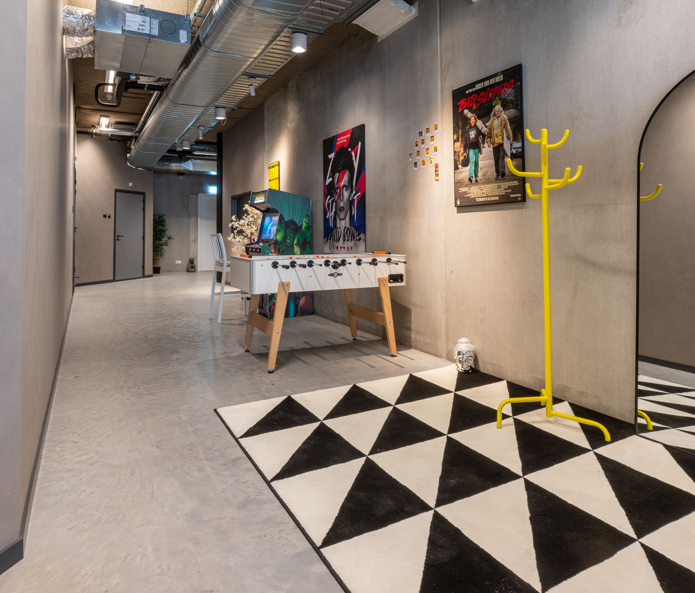 Gang in de studio's van TFA met een zwart-witte vloer, een gele kapstok en een tafelvoetbaltafel