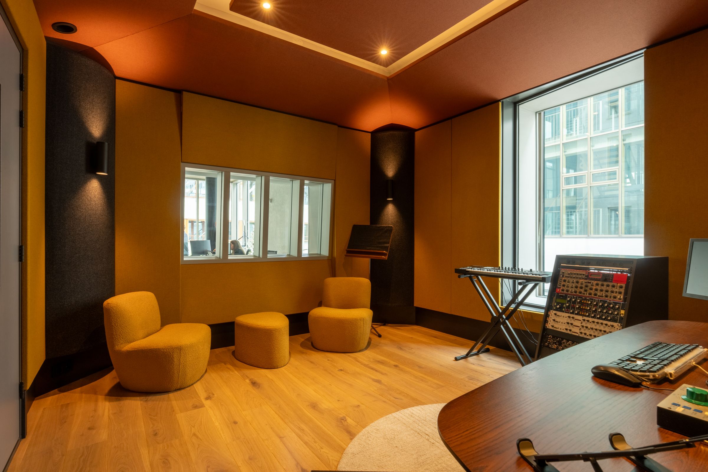 Lounge van een TFA-studio met oranje fauteuils, een keyboard en een groot raam