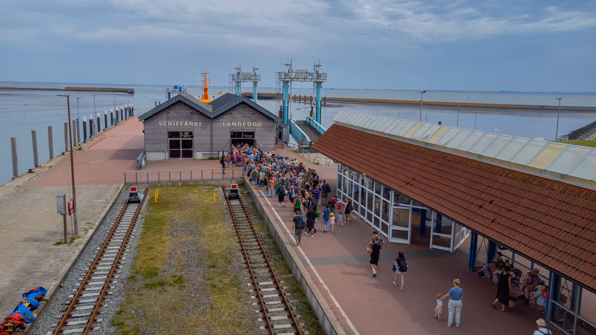 Menschenmenge wartet am Hafen Langeoog auf die Fähre bei bewölktem Himmel.