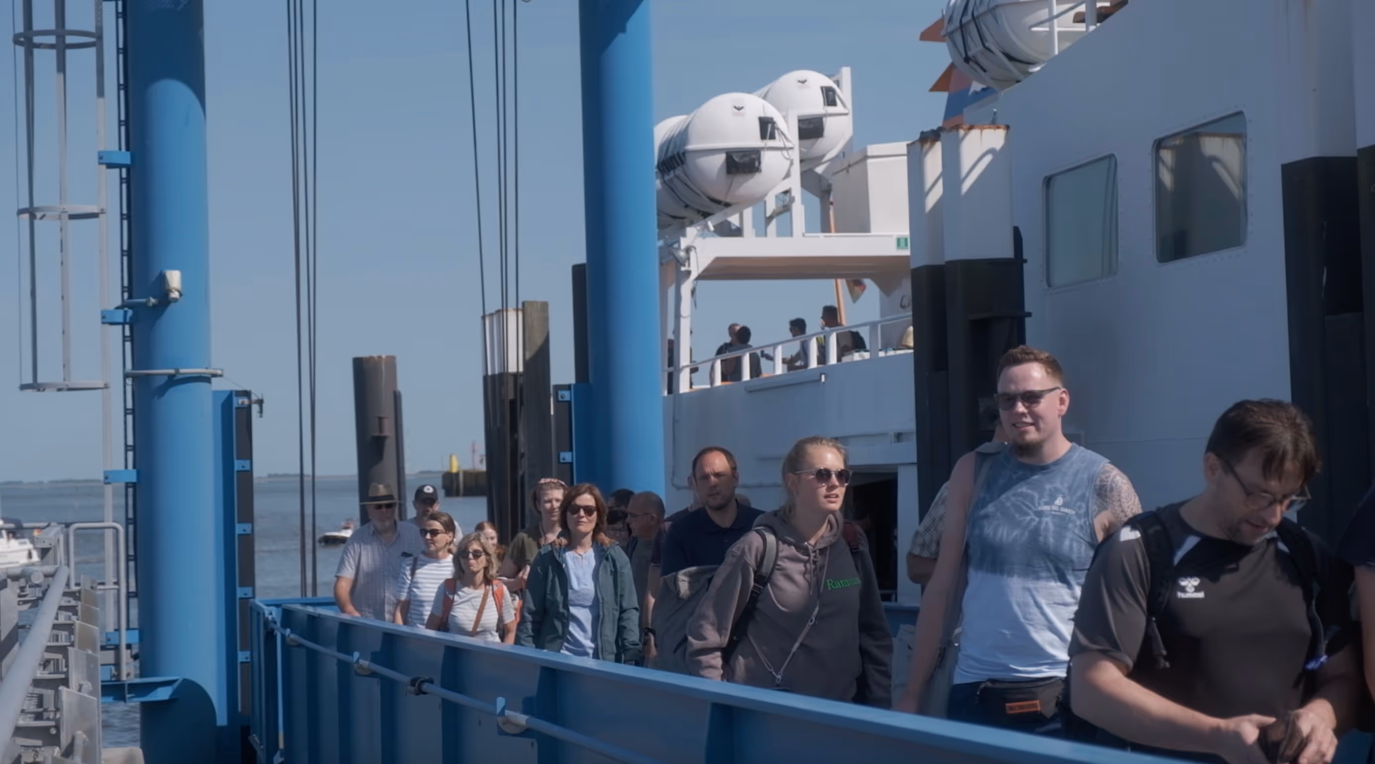 Menschen steigen bei sonnigem Wetter von einer Fähre am Hafen auf Langeoog aus.