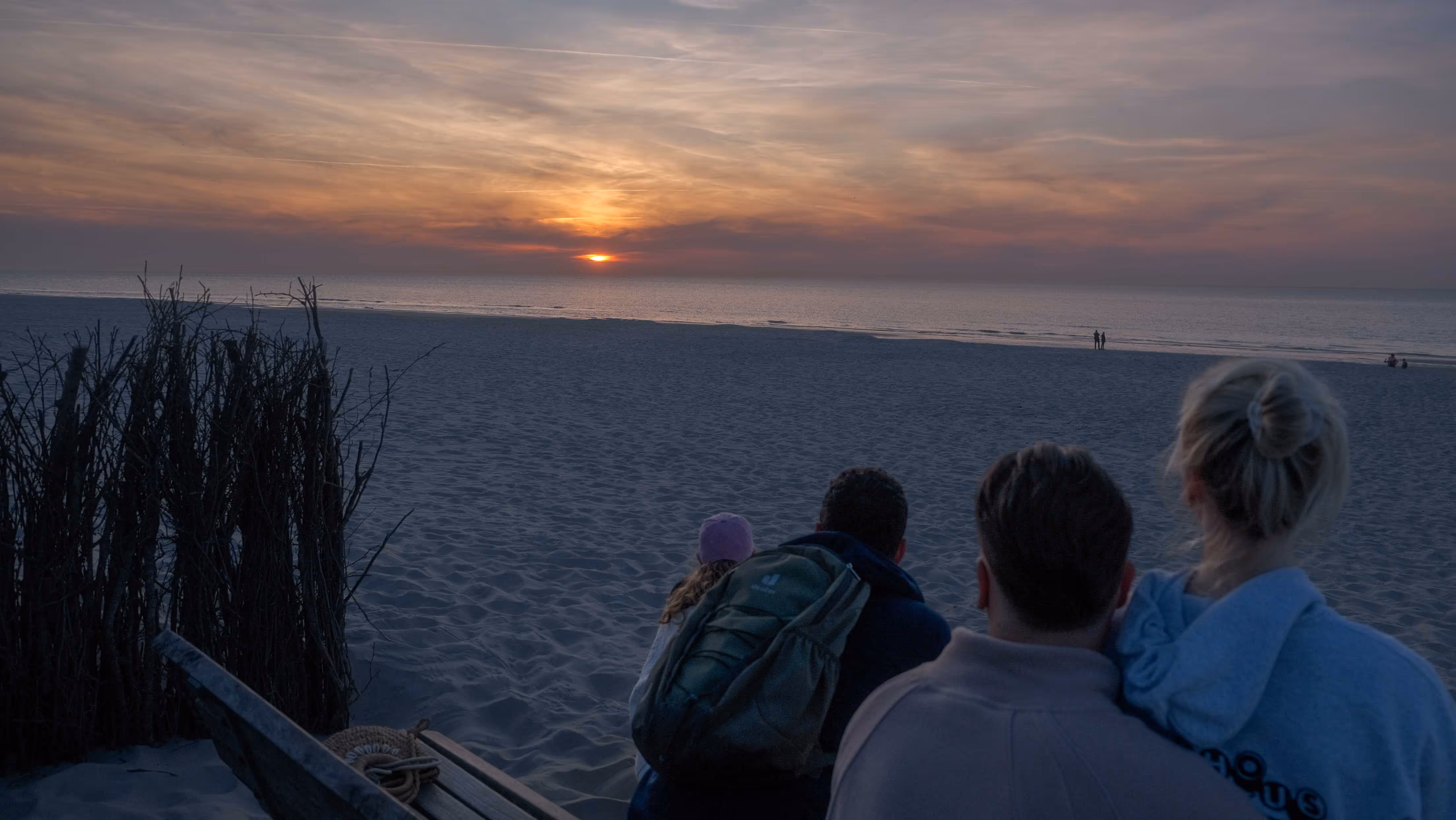 Vier Personen sitzen am Strand und beobachten den Sonnenuntergang über dem Meer von Langeoog.