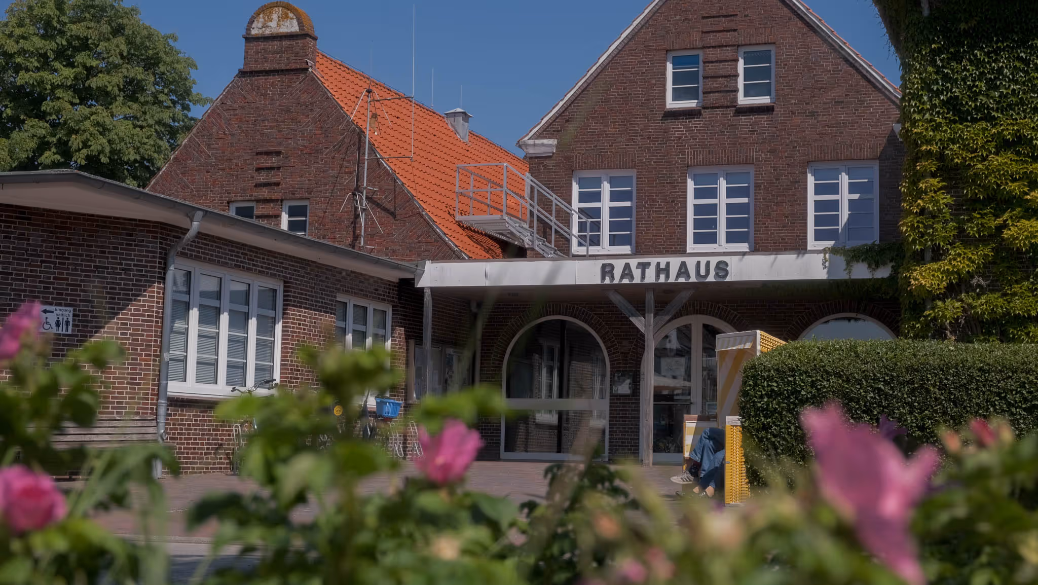Backsteingebäude mit dem Schriftzug "Rathaus" über dem Eingang und Blumen im Vordergrund.