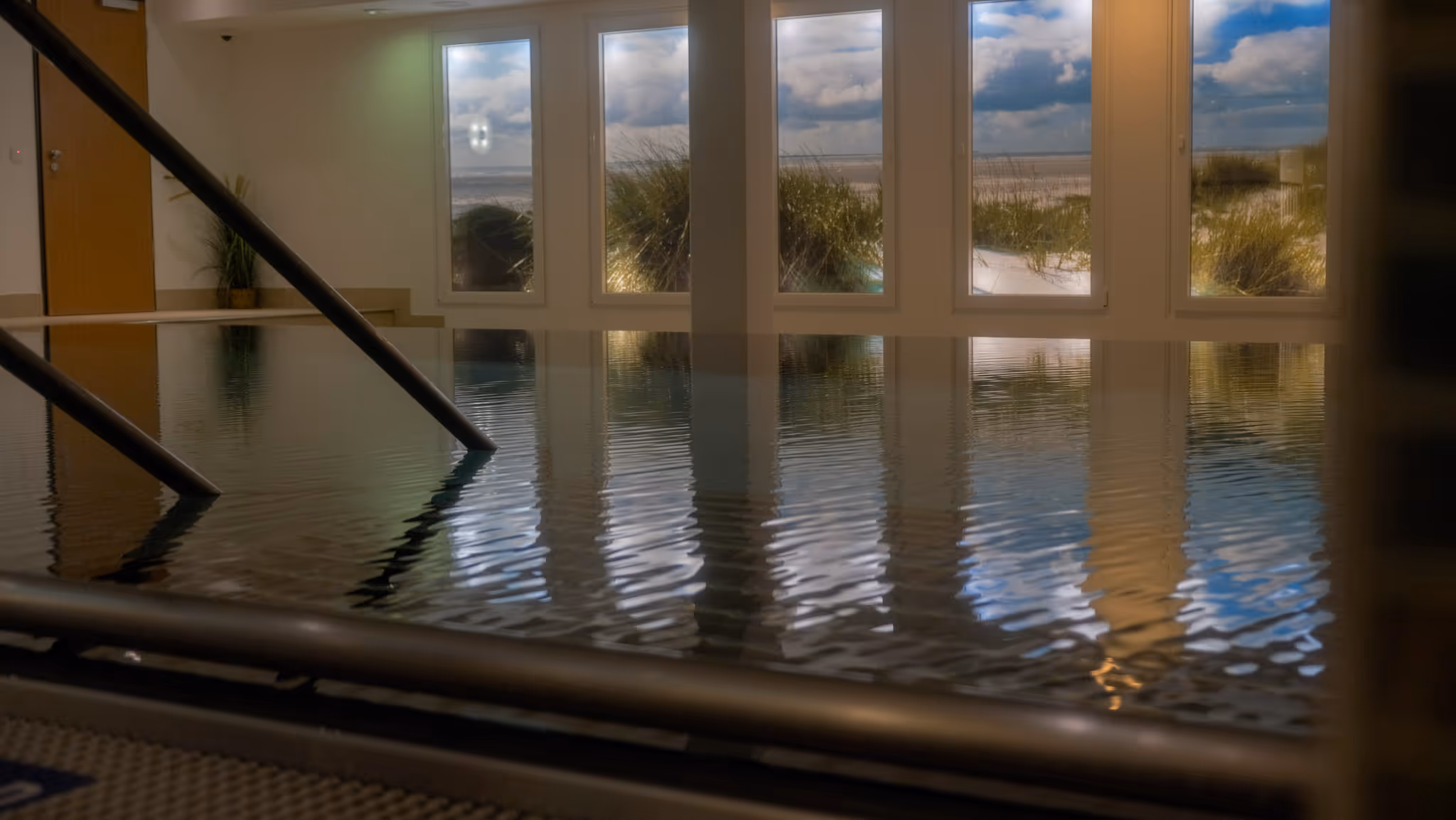 Innenpool mit Reflexionen eines fensterblicks auf Dünen und Himmel.