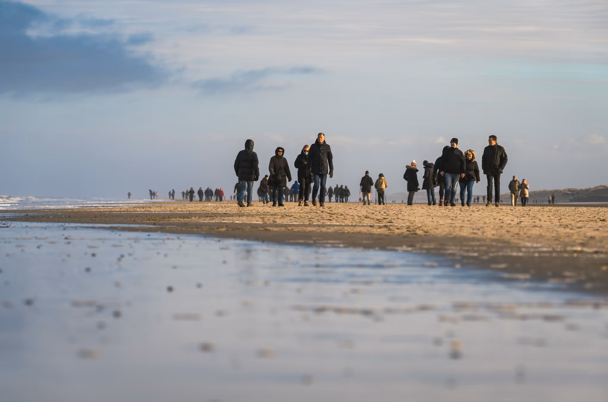Menschen in Winterkleidung spazieren an einem bewölkten Tag am Strand entlang.