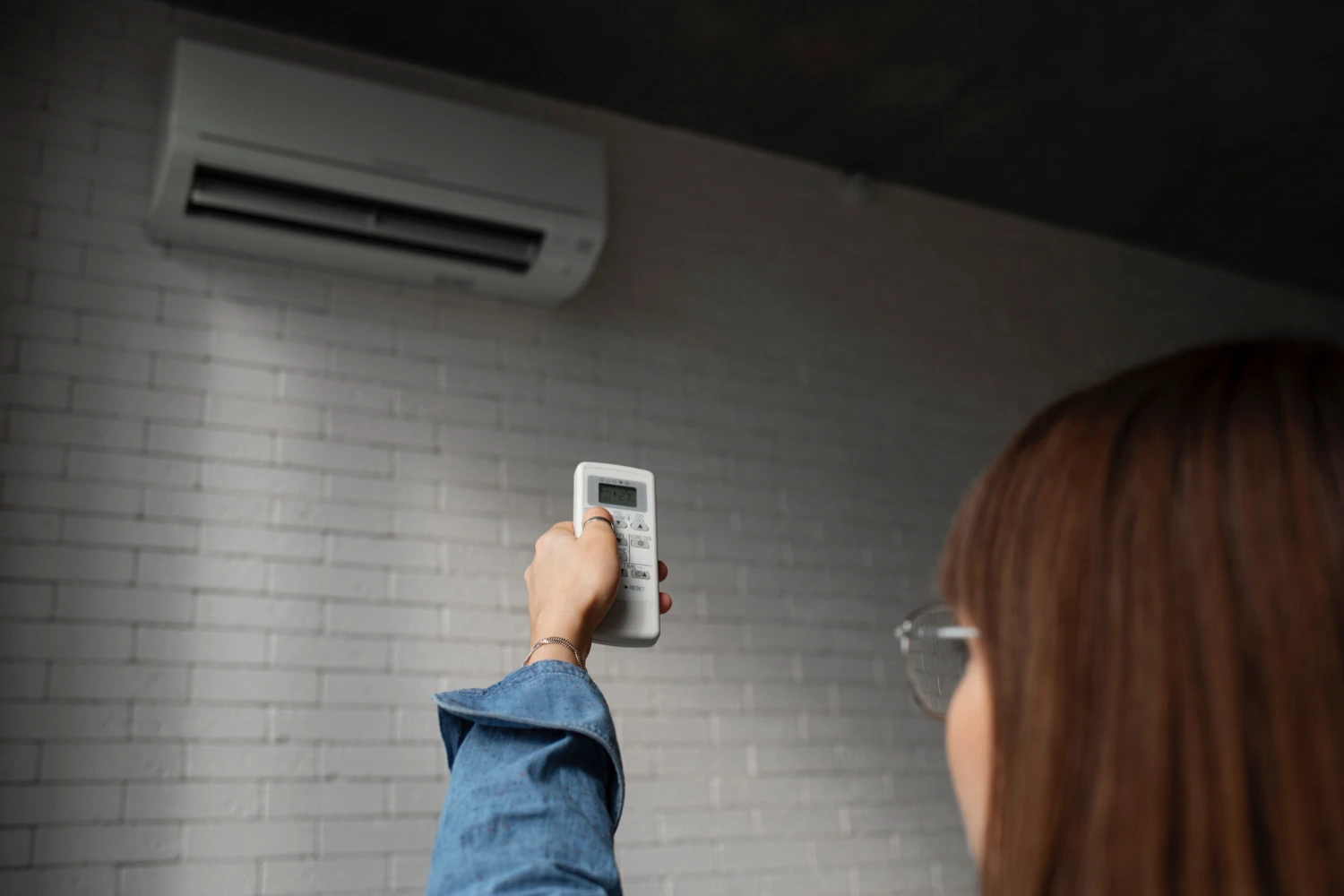 Person adjusting air conditioner with remote control on brick wall