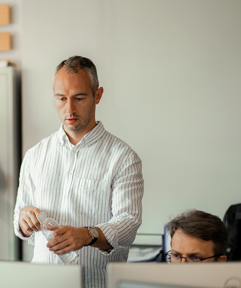 Man pointing at computer screen while discussing work with colleague