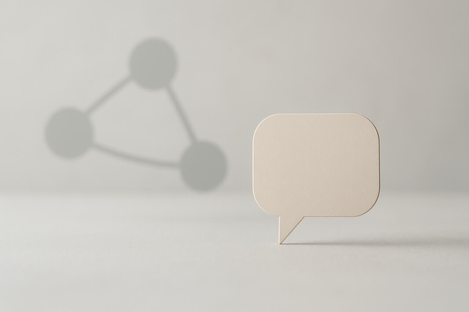 A beige speech bubble cutout stands upright on a light surface with three connected gray circles in the background.