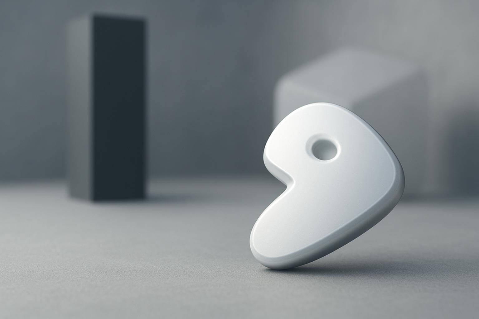A white, abstract, three-dimensional shape with a hole stands upright on a gray surface with blurred shapes in the background.