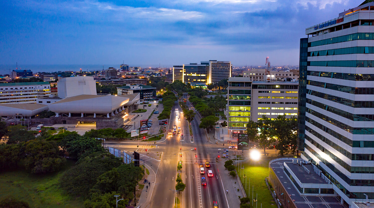 A wide city view at dusk shows busy streets, modern office buildings, and a unique white structure with angular shapes.