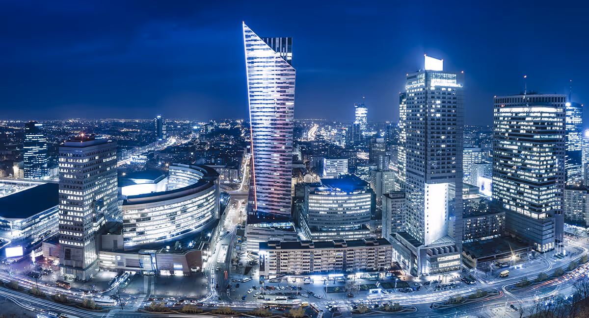 A cityscape at night featuring modern high-rise buildings illuminated by artificial lights.