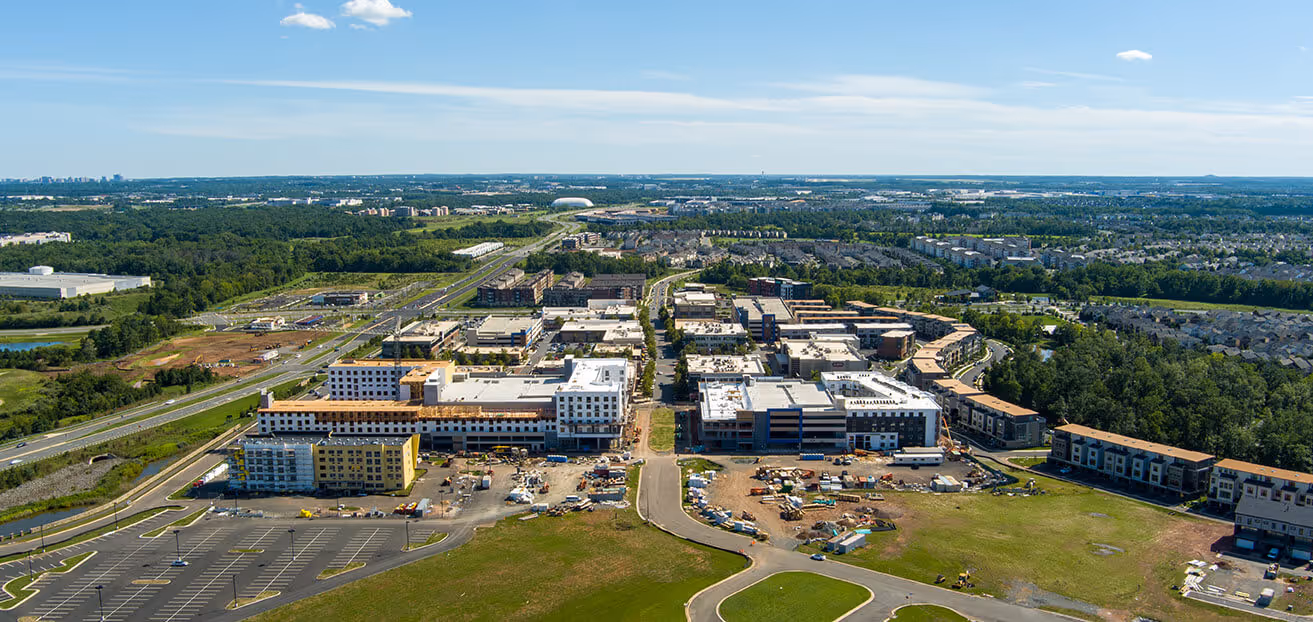 Aerial view of a large complex of multi-story buildings under construction surrounded by parking lots and green areas.