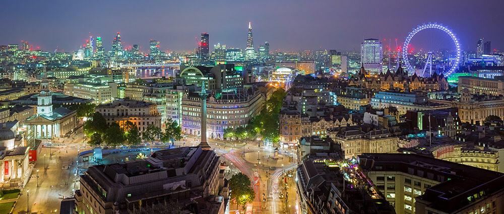 Cityscape at night with illuminated buildings, busy streets, and a large Ferris wheel in the background.