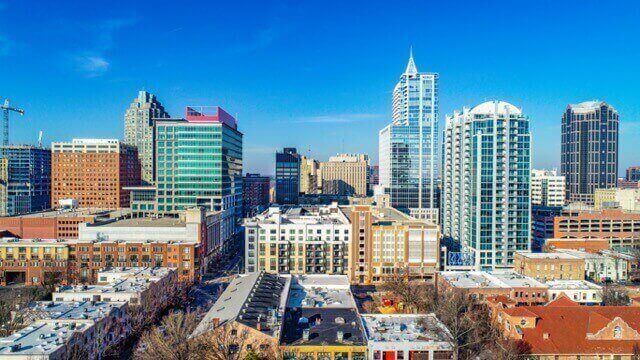A city skyline with a mix of modern high-rise buildings and mid-rise structures under a clear blue sky.