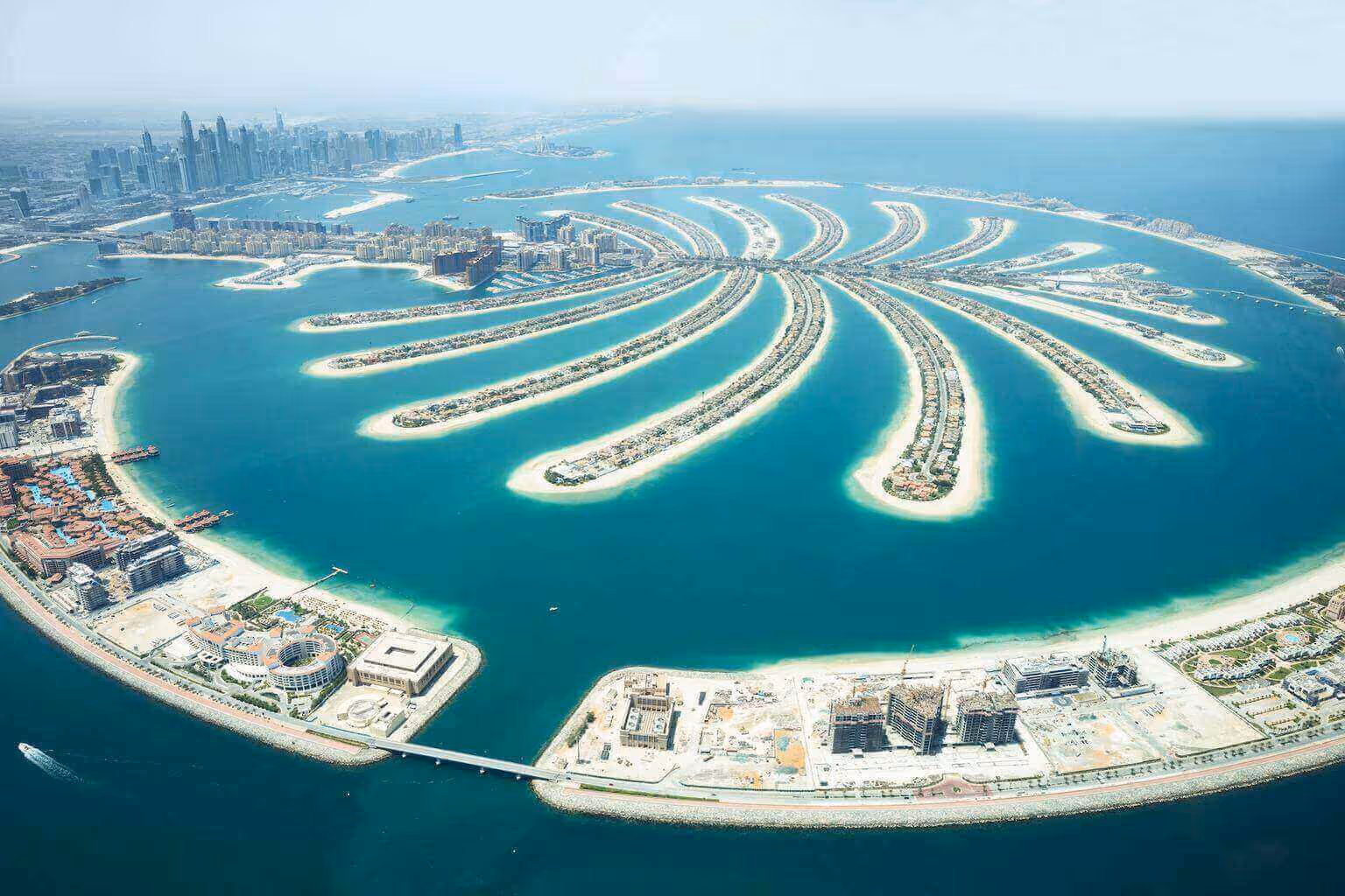 Aerial view of a coastal city with a large, palm-shaped artificial island and numerous buildings along the shore.