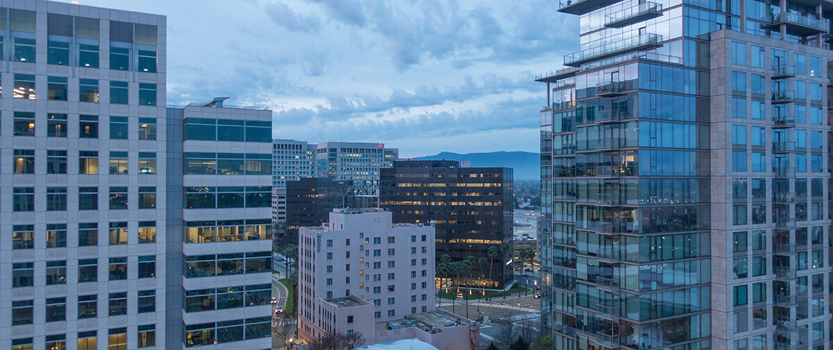 A cityscape with several modern high-rise office buildings at dusk under a cloudy sky.