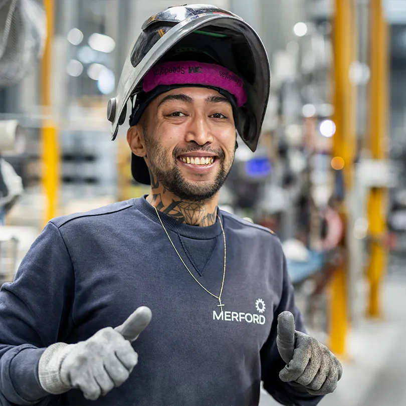 Smiling Merford welder giving thumbs up while wearing protective gear inside the production hall.