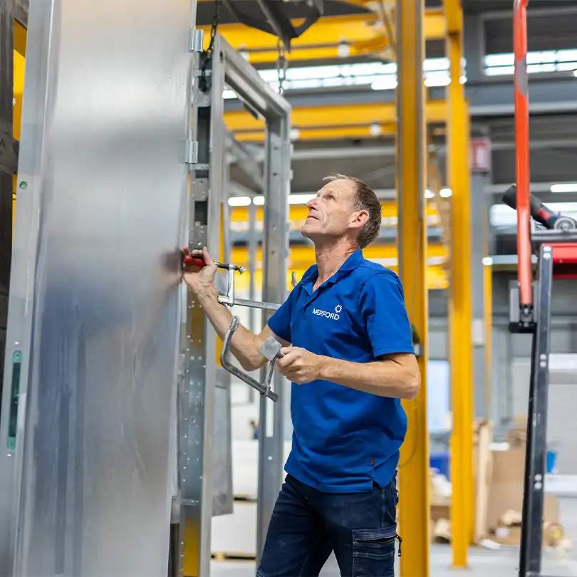 Merford production worker assembling a large steel door inside the factory workshop.