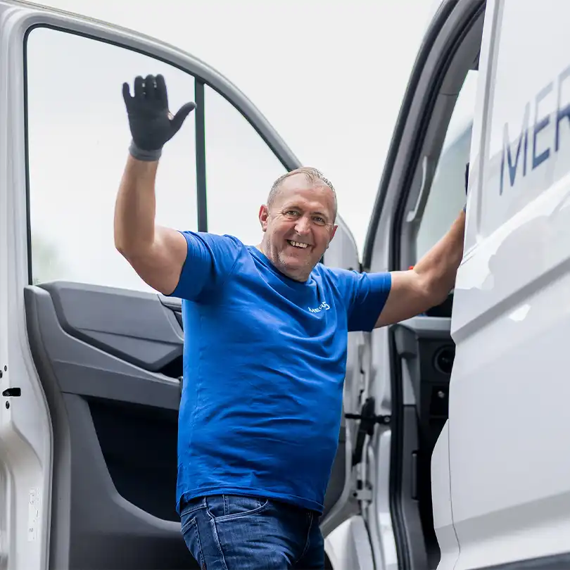 Merford installer smiling and waving while stepping out of a company van at a project site.