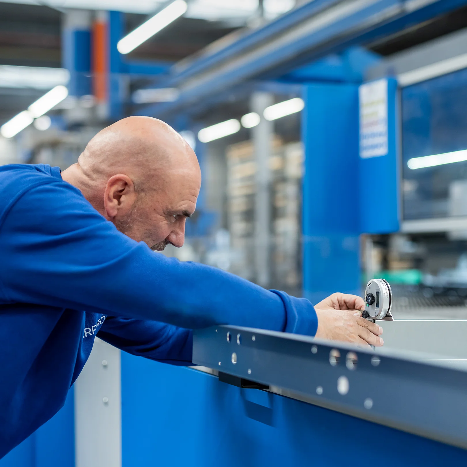 Employee in a blue uniform carefully measuring a metal component in a modern production facility, illustrating precision and craftsmanship at Merford.