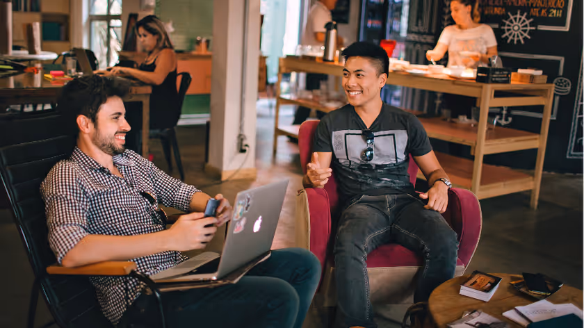 Two men chatting with laptops in a casual co-working space