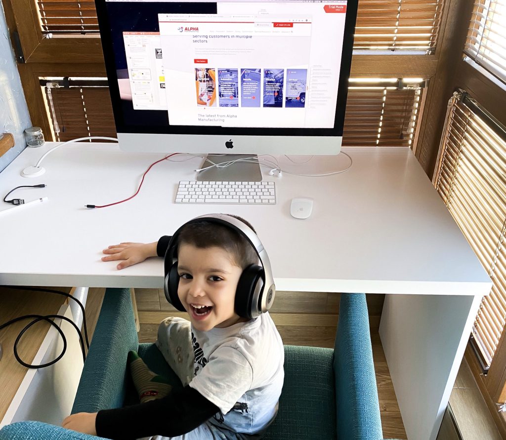 Smiling child wearing headphones, with a computer in the background