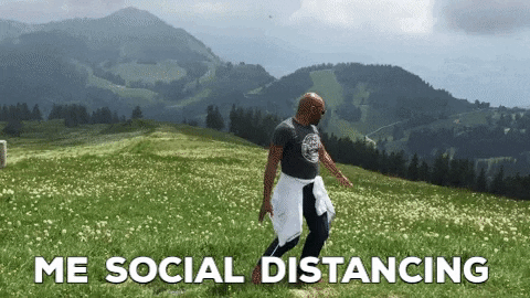 Man happily spreading his arms wide in a field, captioned 'Me Social Distancing