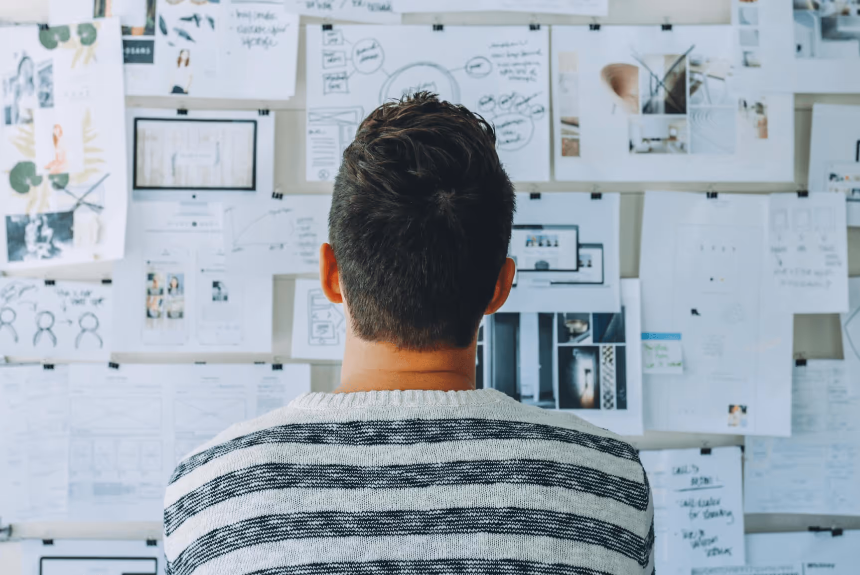 Person in a striped sweater looking at a wall filled with notes and sketches of essence of personas.