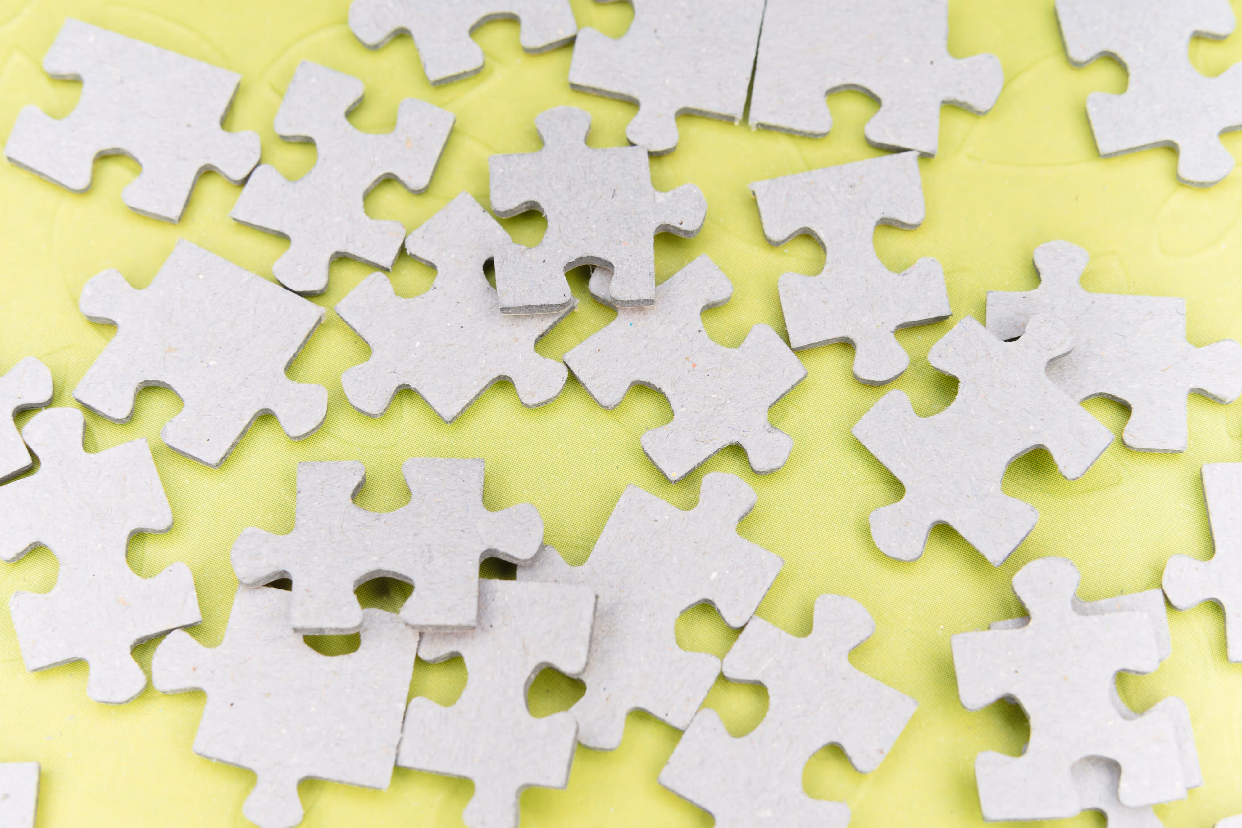 Several gray jigsaw puzzle pieces scattered on a yellow surface telling about perfect agency-design fit.