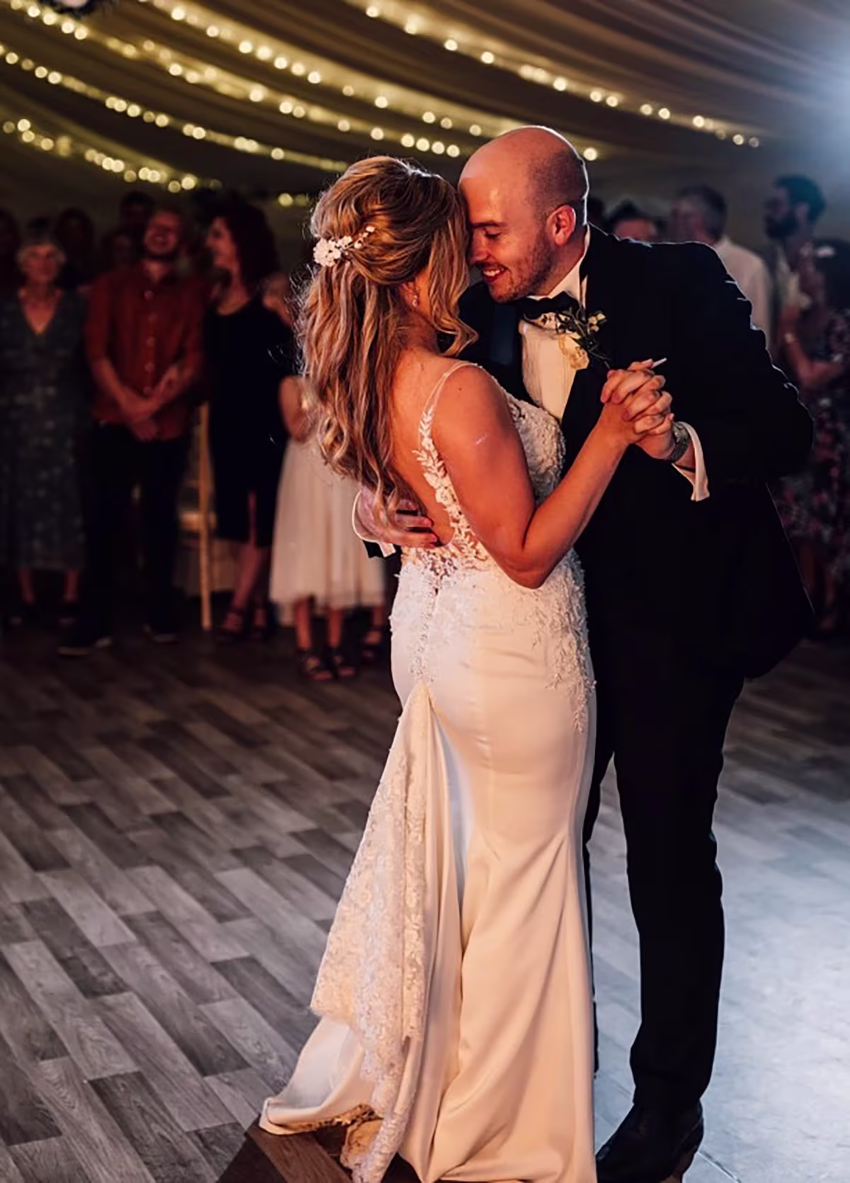 Bride and groom smiling and dancing closely at their wedding reception under string lights.