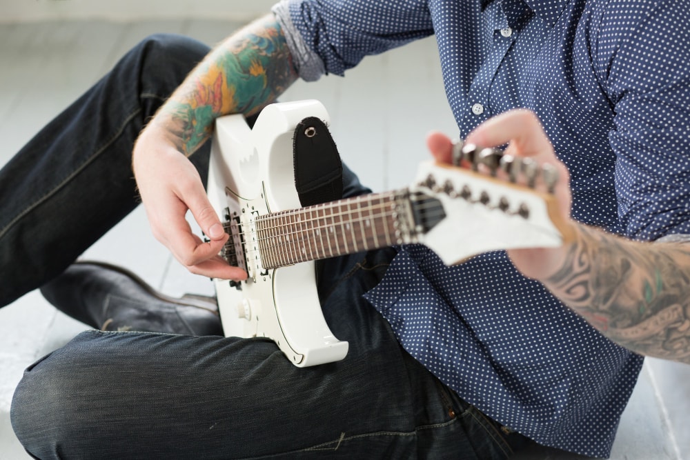 Man sat on the ground as he joins his guitar