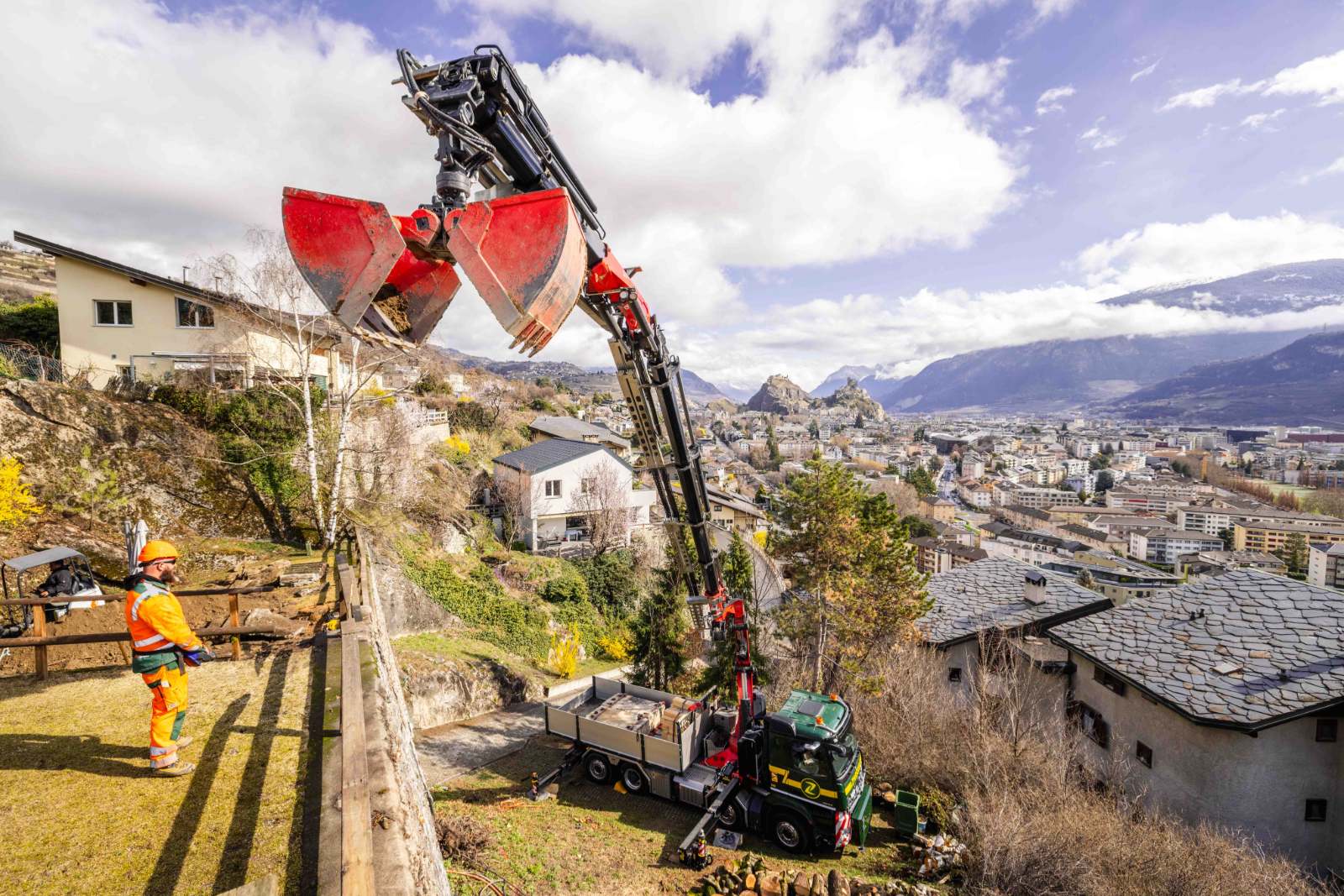 Camion-grue Zwissig déchargeant du matériel avec une benne preneuse, au-dessus de la ville