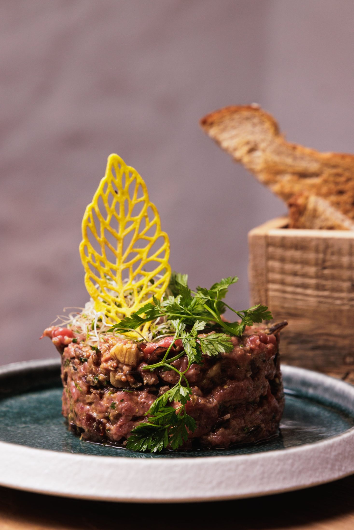 Tartare dressé sur une assiette bleue, avec une tuile décorative