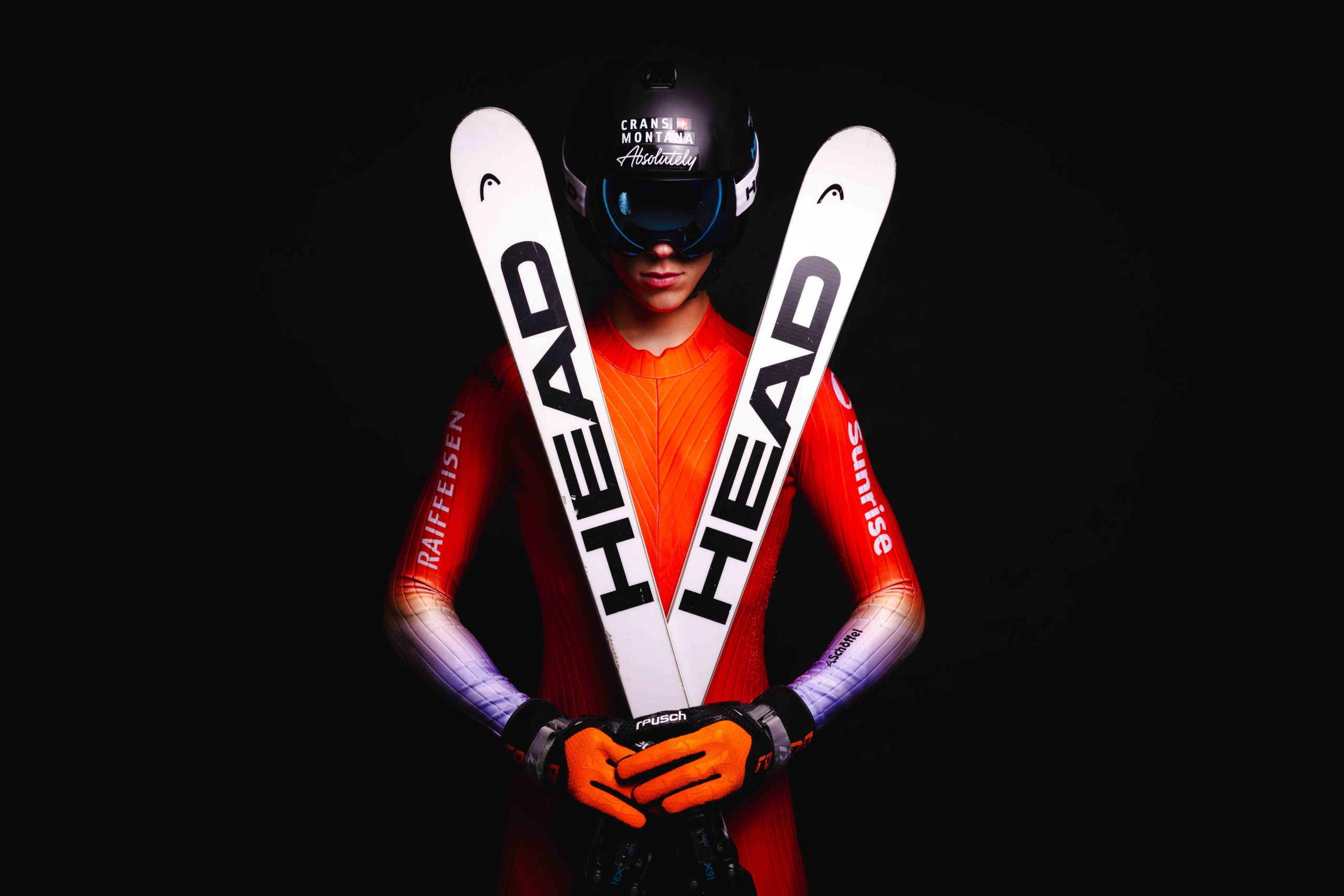 Le skieur James Ketteridge en combinaison orange, skis Head croisés devant lui, en studio