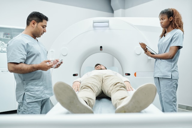 Patient undergoing a CT scan with two medical professionals standing by the scanner.