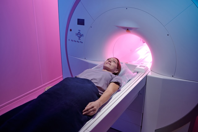 Patient lying inside an MRI machine during a scan, illuminated by soft pink lighting.