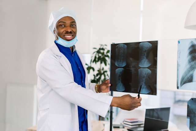 Healthcare professional smiling while holding and pointing to an X-ray film.