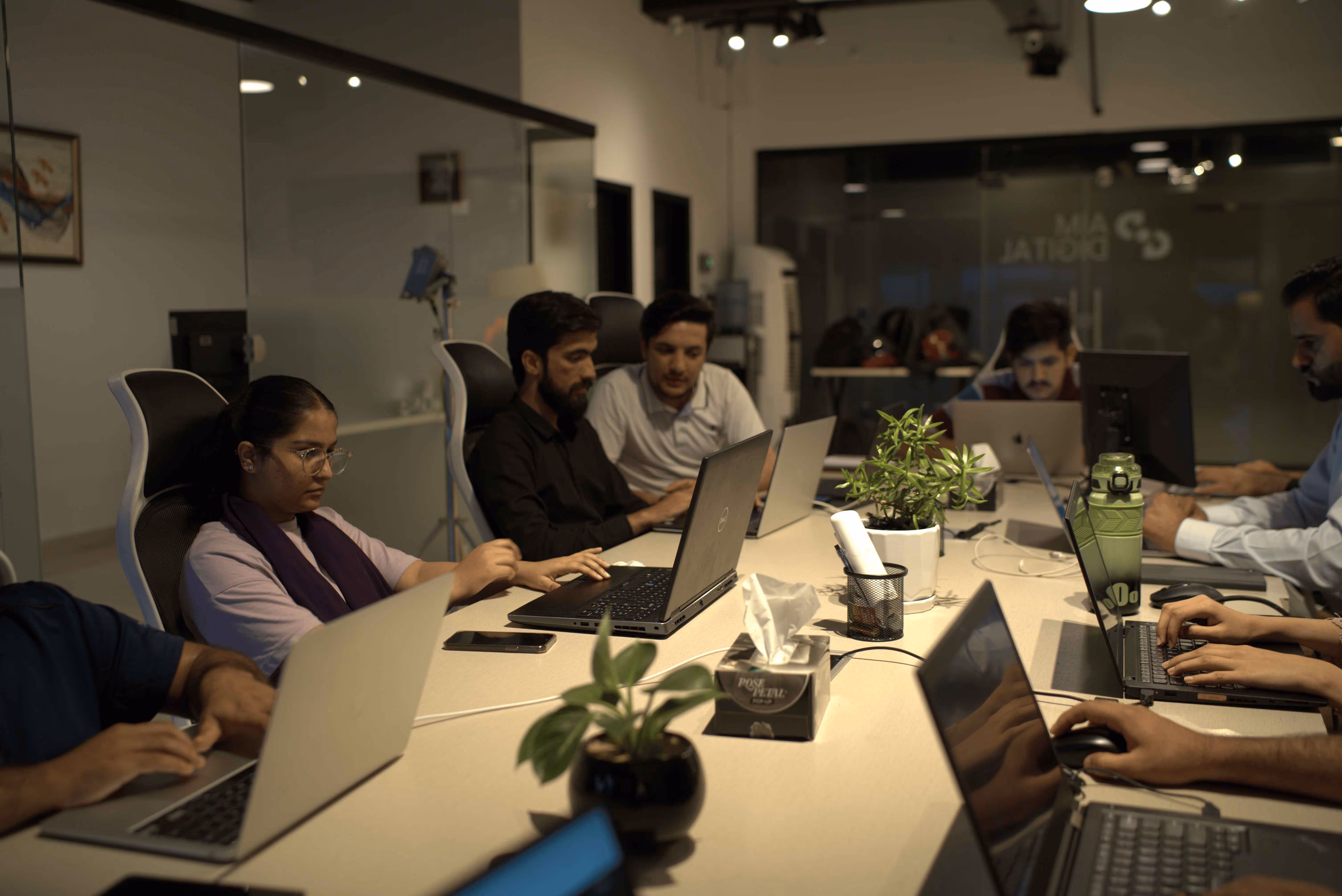 A group of professionals working on laptops around a conference table in a modern office.