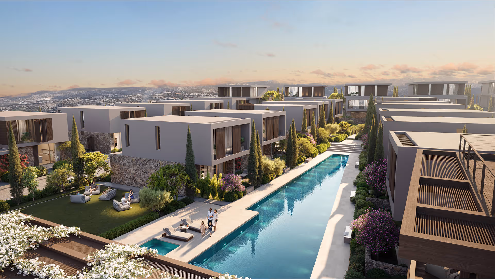 Modern villa community with a long pool, lounge chairs, landscaped gardens, and people relaxing outdoors.
