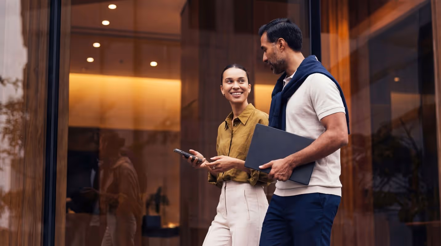 Two business professionals smiling and walking outside a modern office building.