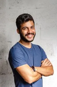 Photo of a candidate. Young man wearing blue t-shirt, smiling with crossed arms.