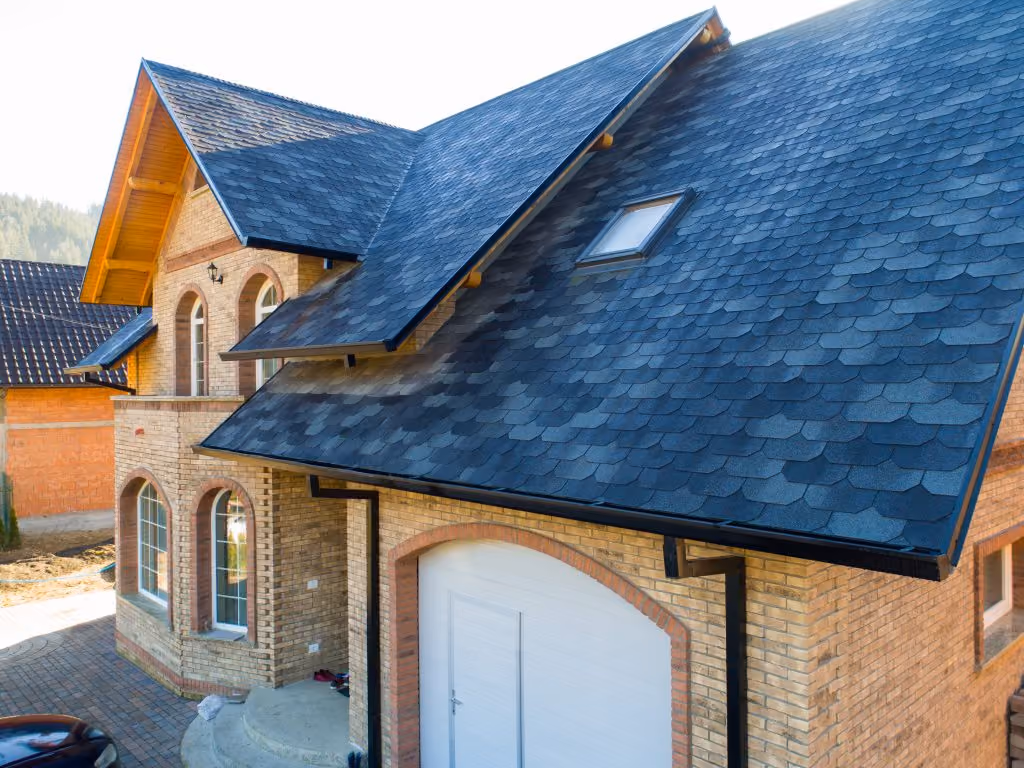 Brick house with large blue-gray shingled roof, arched windows, white garage door, and a small skylight.