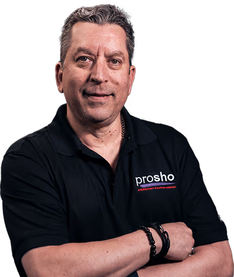 Man with short gray hair wearing a black polo shirt with 'prosho' logo and folded arms.