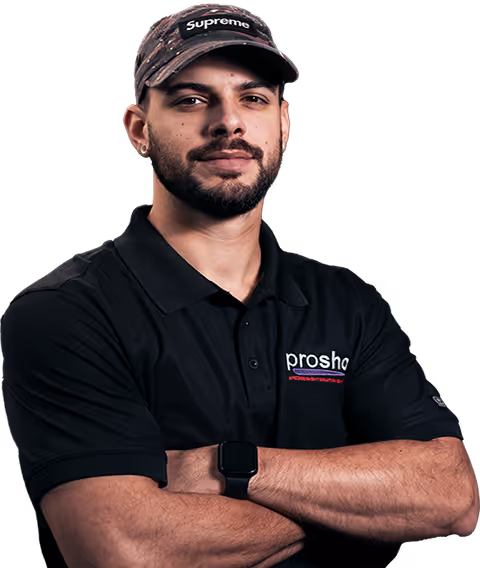 Man with beard wearing a Supreme cap and a black Proshop polo shirt with arms crossed.