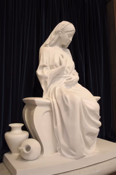 White marble statue of a seated woman in flowing robes with two vases on the ground beside her.