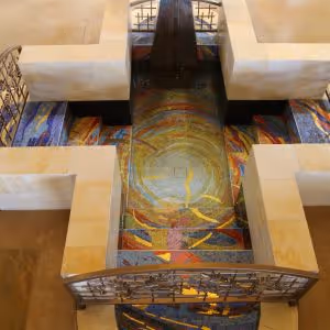 Bird's-eye view of a cross-shaped architectural structure with a colorful mosaic floor and metal railings.